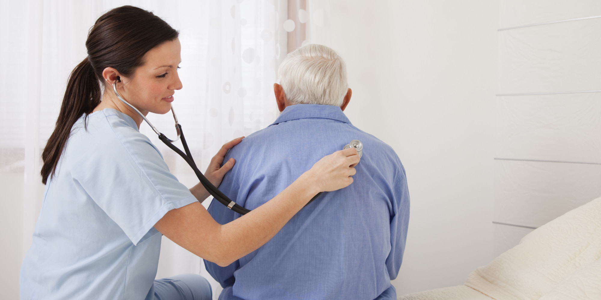 A nurse using a stethoscope on the back of a patient listening carefully for any issues.